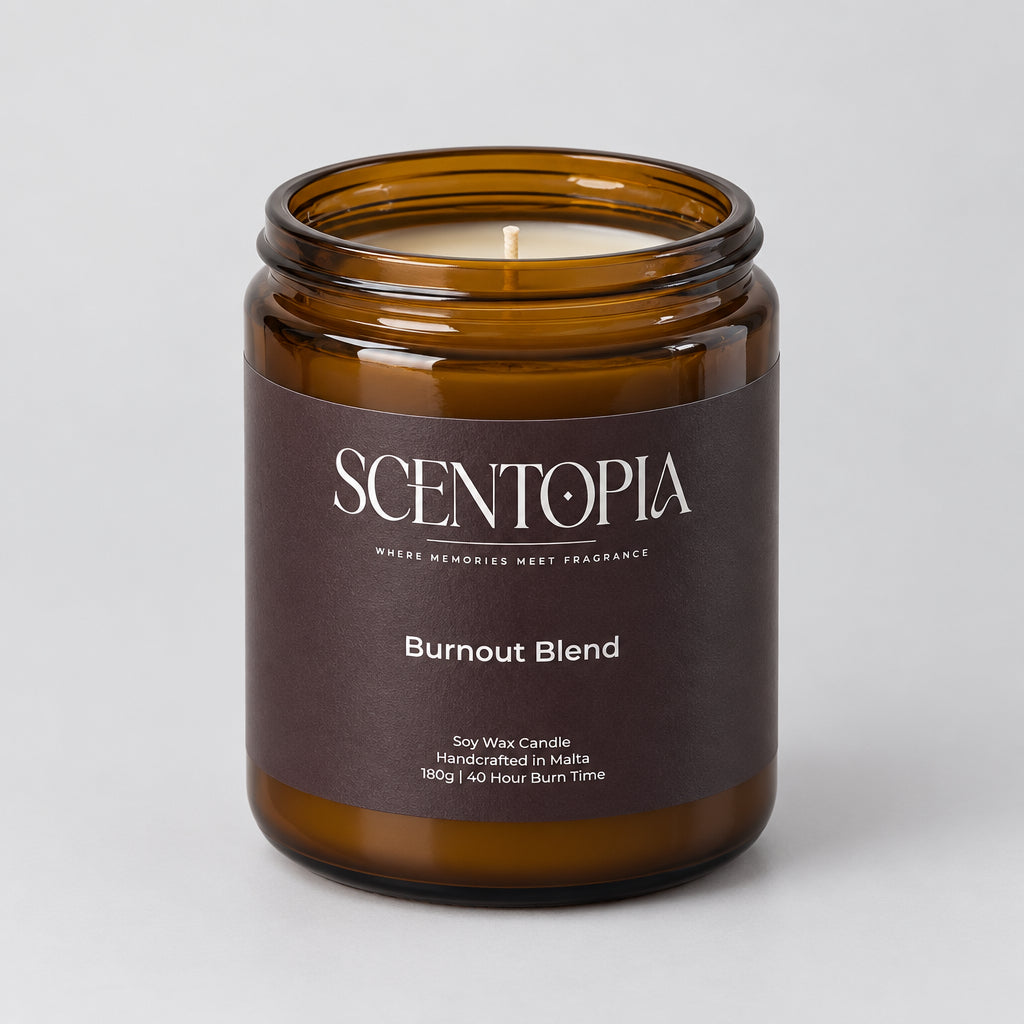 An amber glass jar candle with a dark brown label reading 'SCENTOPIA Burnout Blend' sits on a wooden surface against a plain light background.
