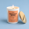 Candle labeled 'Burnout Blend' with a gold lid on a light blue background