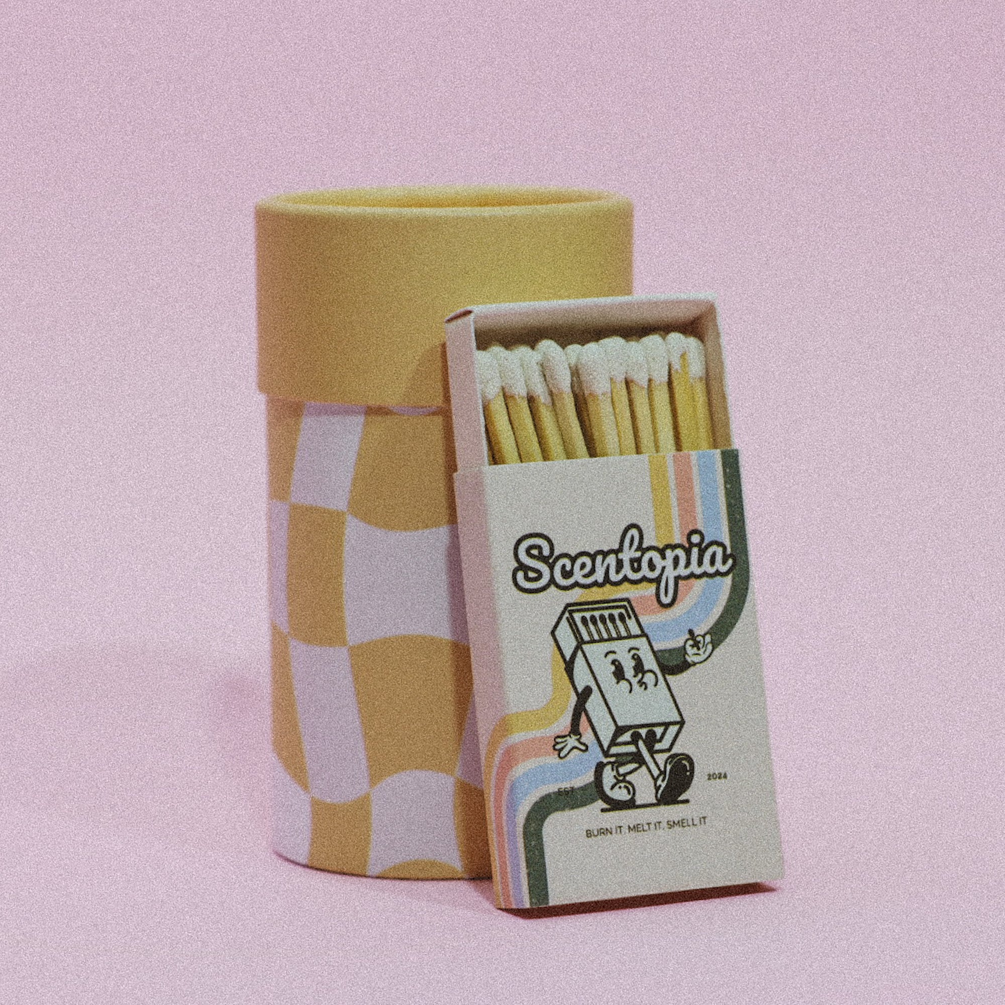 A yellow and white checkered matchbox with a cartoon scent cone on the lid, containing a pack of matches. The brand 'SCENTOPIA' is visible on the packaging.