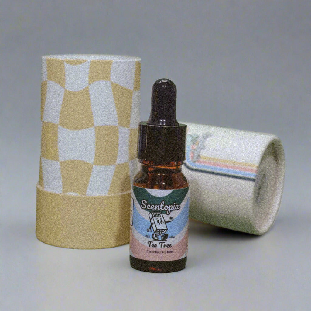 A 10ml amber dropper bottle of Scentopia Tea Tree essential oil stands in front of a tall cylindrical tube with a yellow and white retro checkerboard pattern, placed on a green surface.