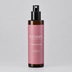 A bottle of Scentopia 'Cried But Still Cute' room spray, featuring a dusty pink label and a black spray nozzle, set on a wooden surface against a plain light background.