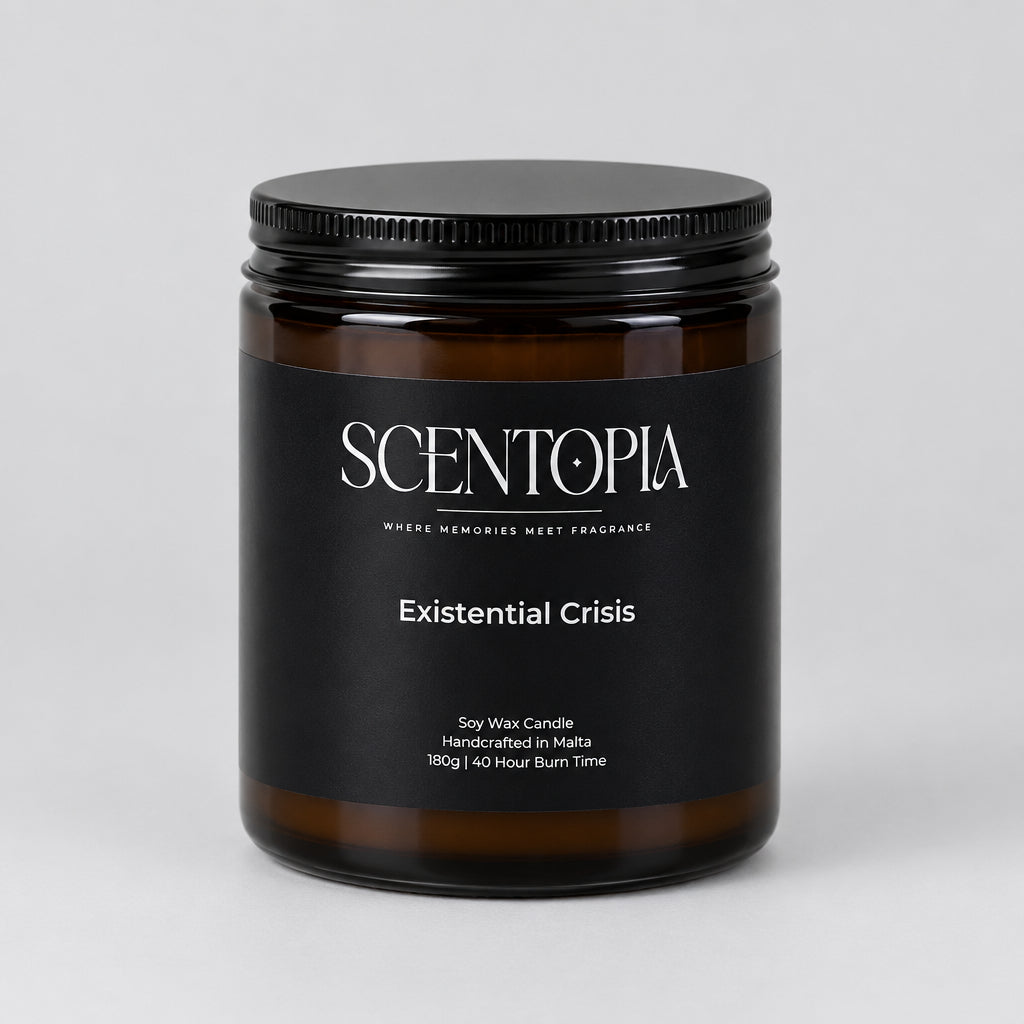 A SCENTOPIA soy wax candle in a dark amber glass jar with a black lid, labeled 'Existential Crisis', sitting on a wooden surface against a plain beige wall.