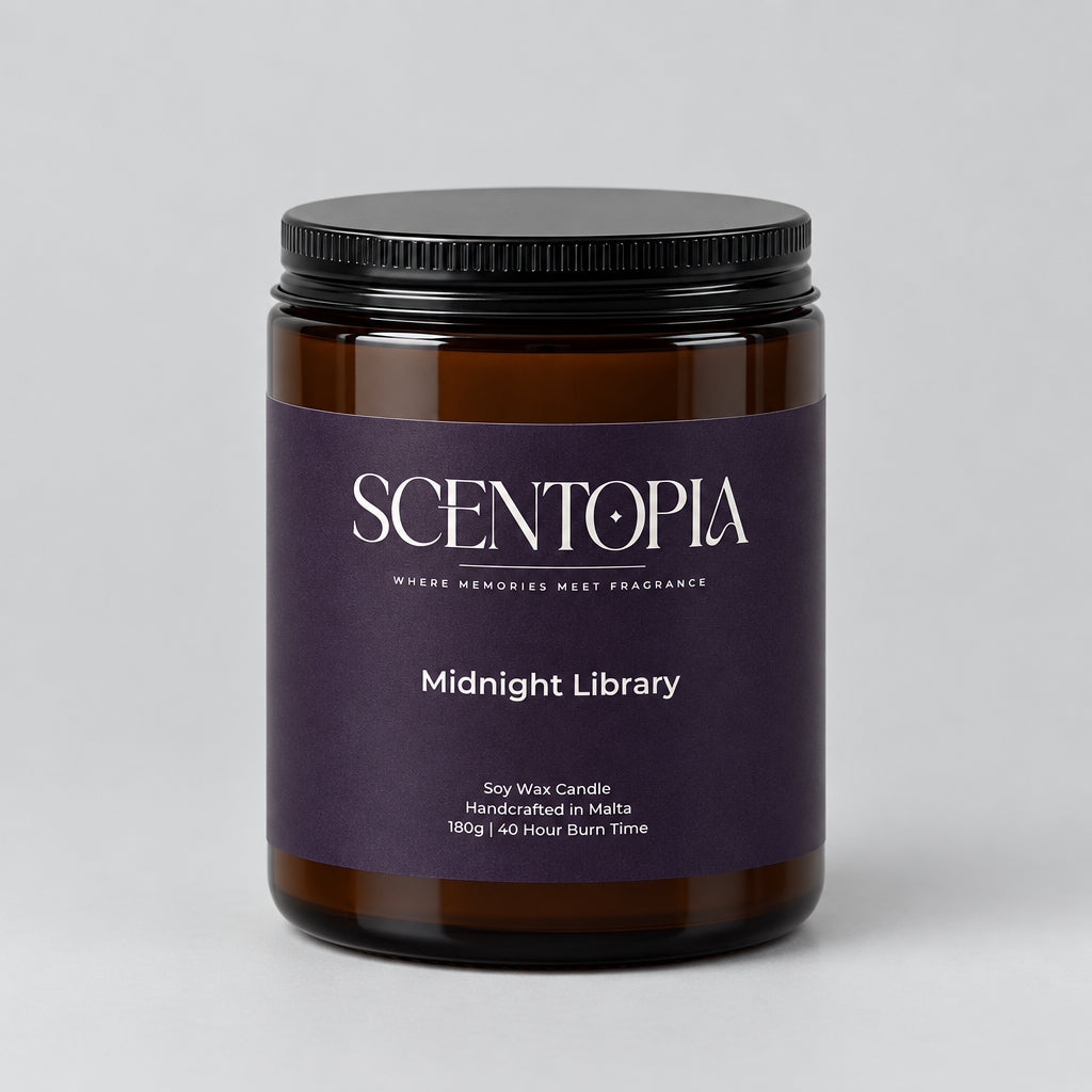 A Scentopia Midnight Library soy wax candle in a dark amber glass jar with a black lid and a dark purple label, sitting on a wooden surface against a plain beige wall.