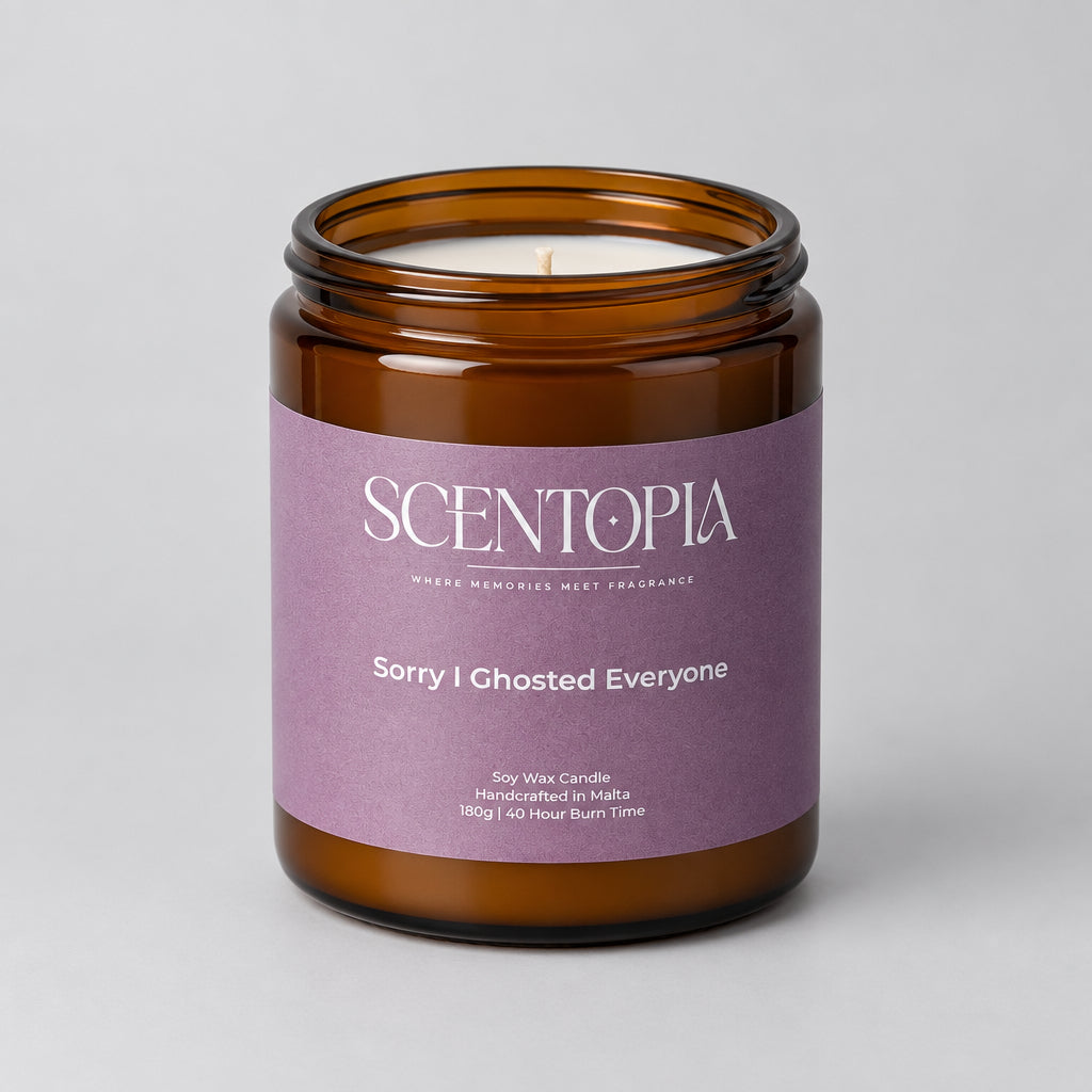 A Scentopia soy wax candle in an amber glass jar with a lavender-purple label reading 'Sorry I Ghosted Everyone,' sitting on a wooden surface against a plain light wall.