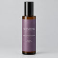 A bottle of Scentopia 'Sorry I Ghosted Everyone' room spray, featuring a dark amber glass bottle, a black cap, and a lavender-purple label, set on a wooden surface against a plain light background.