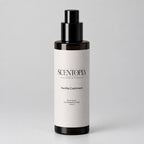 A 500ml bottle of Scentopia Vanilla Cashmere room spray, featuring a dark amber glass bottle, a black pump dispenser, and a light gray paper label, resting on a wooden surface against a plain beige wall.