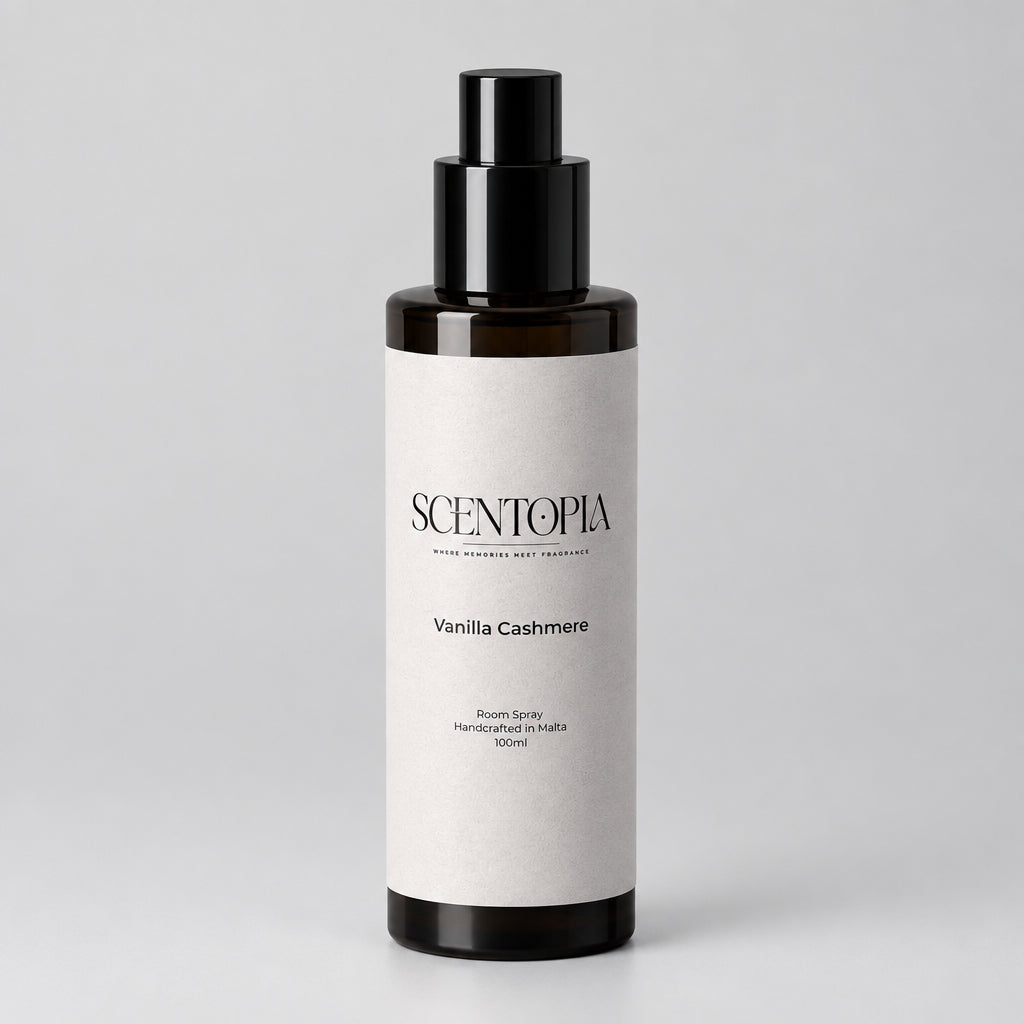 A 500ml bottle of Scentopia Vanilla Cashmere room spray, featuring a dark amber glass bottle, a black pump dispenser, and a light gray paper label, resting on a wooden surface against a plain beige wall.