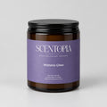 A Scentopia Wisteria Glow scented wax melt jar with a dark purple label and black lid, sitting on a wooden surface against a plain beige wall.